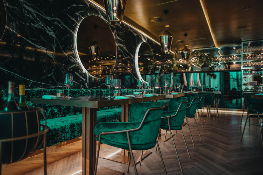 Sfeerafbeelding van Restaurant Goud in Rotterdam van Herman den Blijker, groene stoelen en grote ronde spiegels aan de muur.