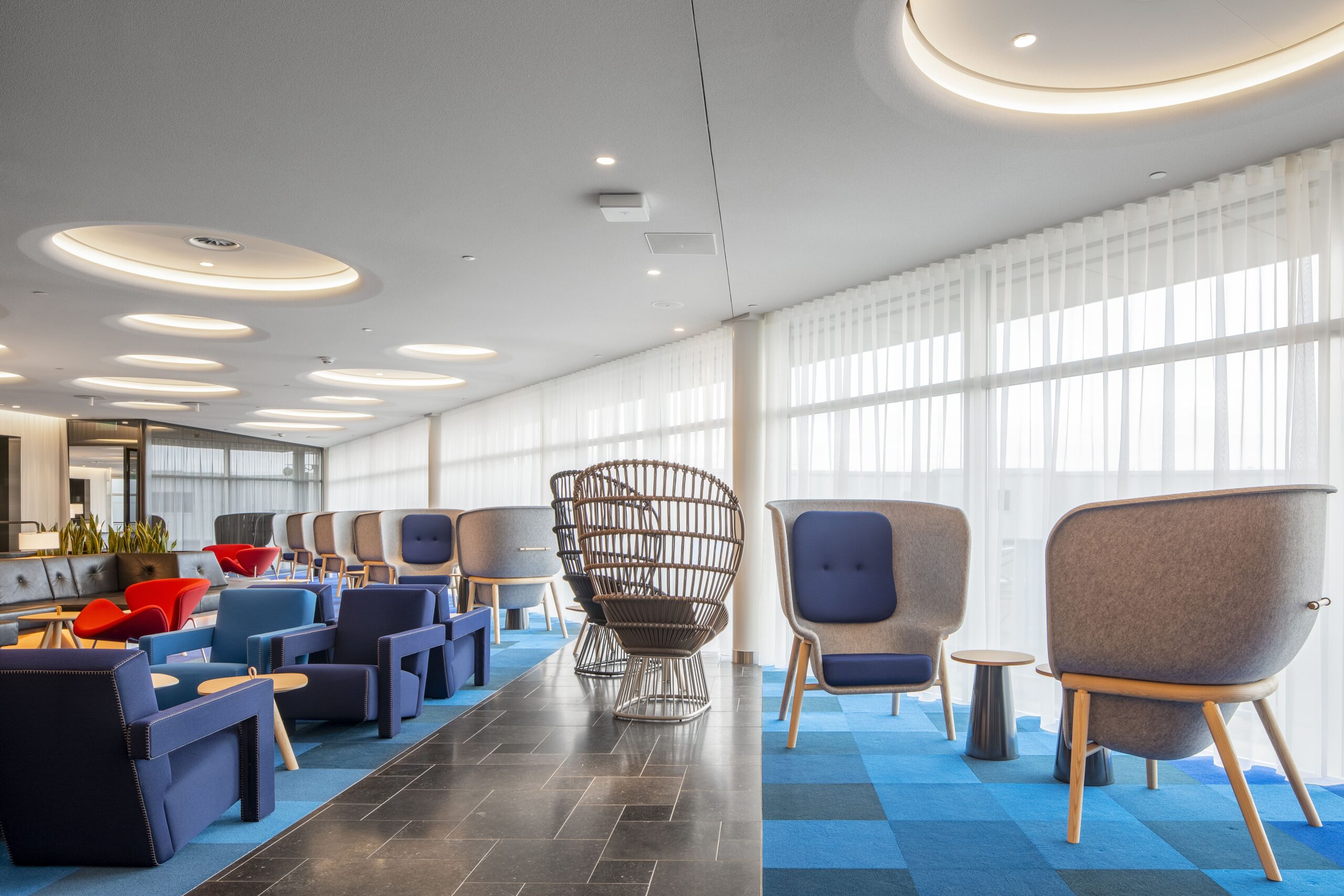 KLM Crown members lounge met hoge, grijze stoelen en en blauw checkered tapijt.