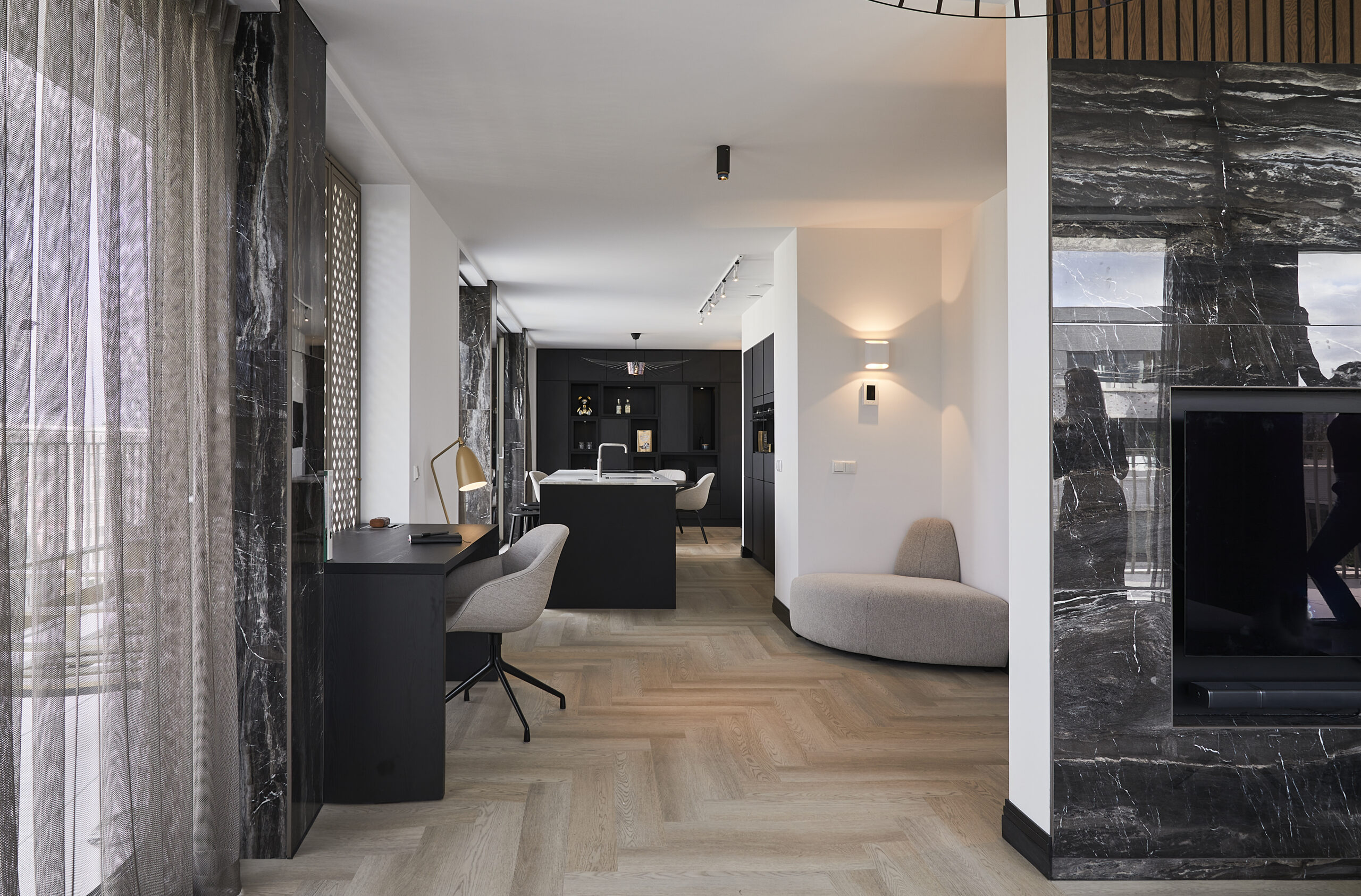 Doorkijk in een appartement met houtkleurige vloer, donkere en beige meubels en lamp aan de wand.