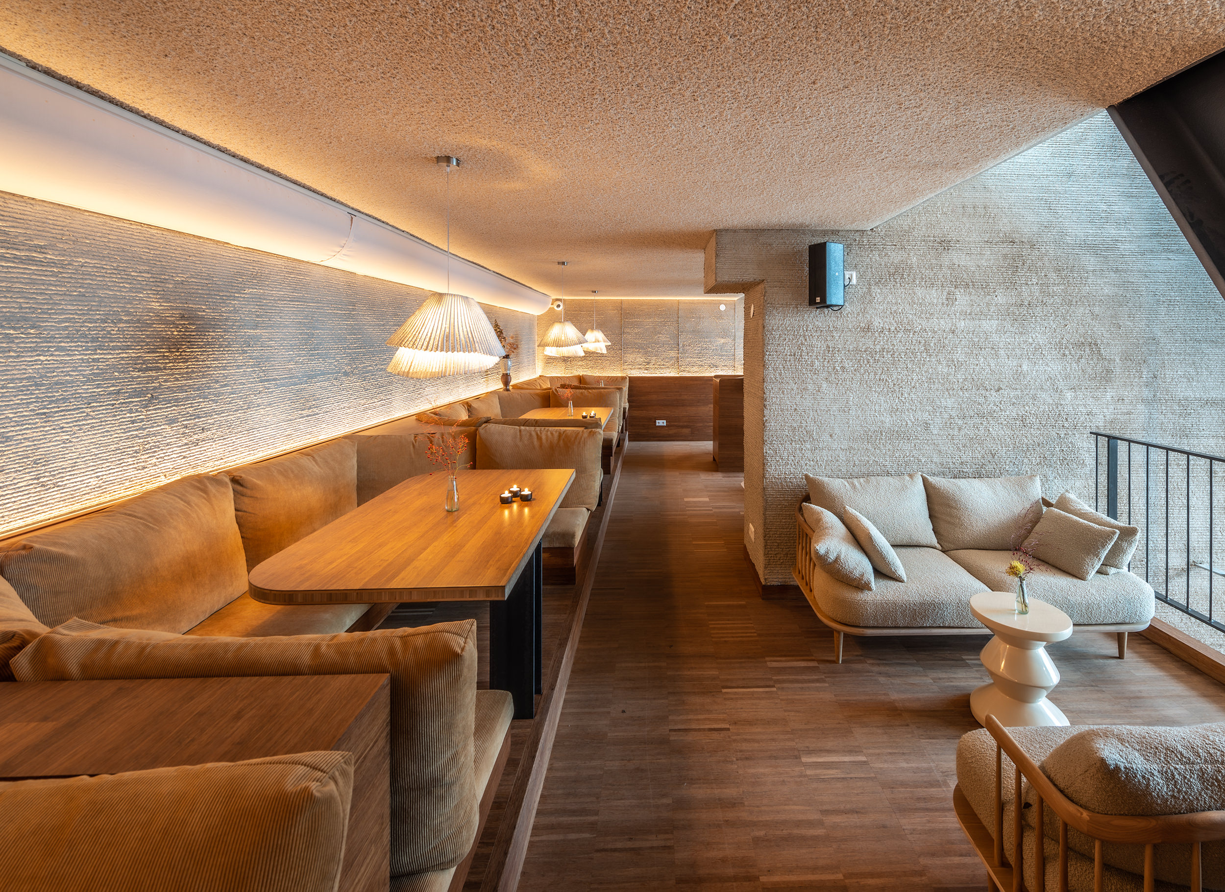 Zitplaats in restaurant Next met een lange bank en kleine poef rechts. Laag plafond met sfeerlicht aan de muur.